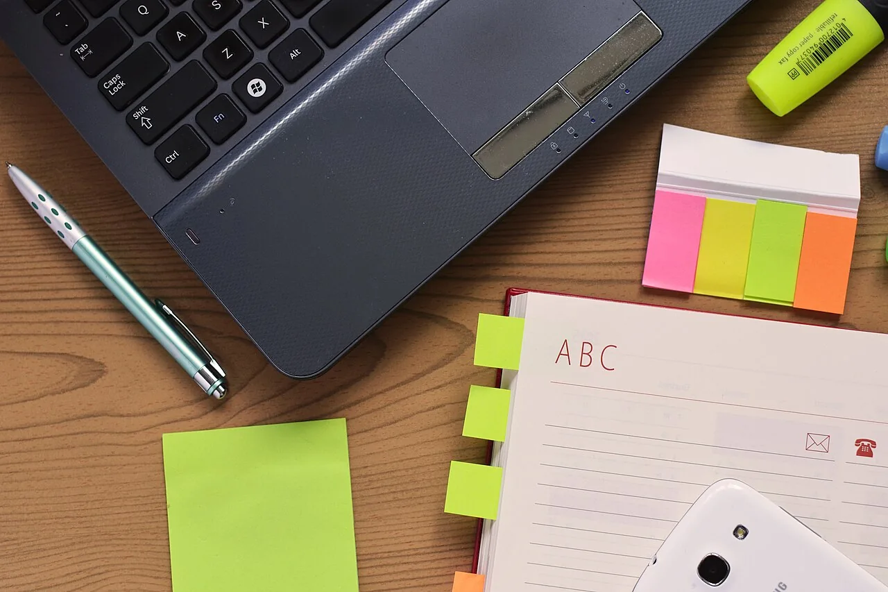 Laptop keyboard, notebook, smartphone, and stationery on a wooden desk