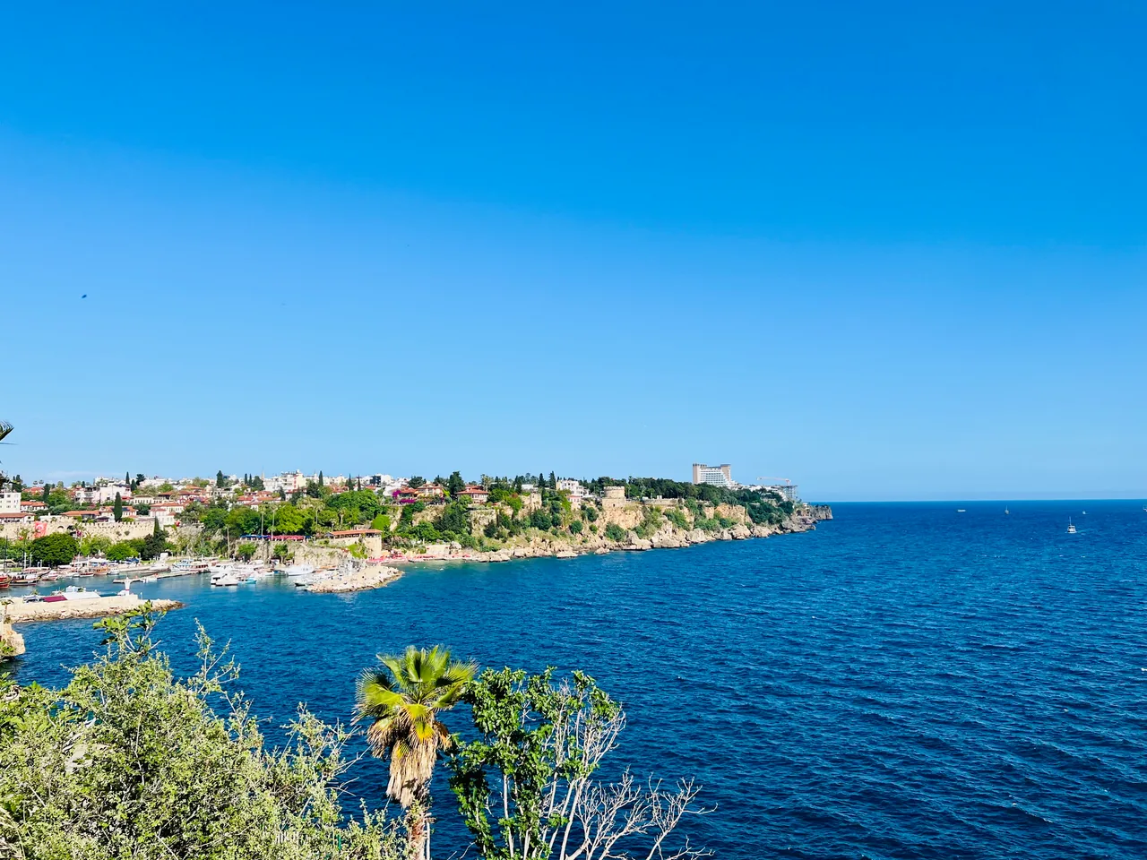 Boats in Antalya harbour beside waterfront cliffs, buildings and the blue Mediterranean Sea